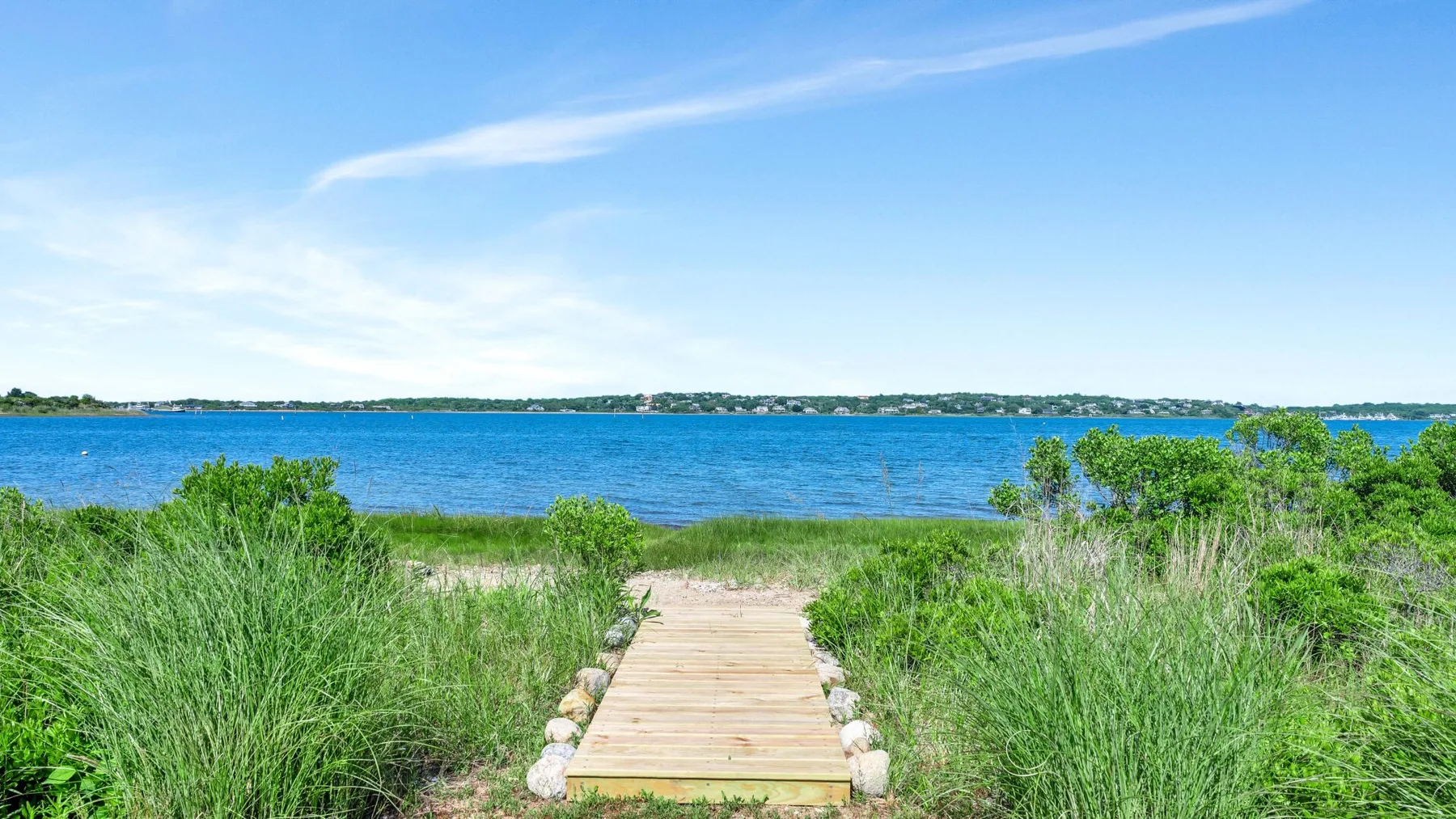 A wooden path leads through tall grass toward a blue shoreline.
