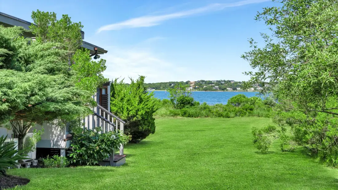 Un jardín con césped junto a una casa da a un lago.