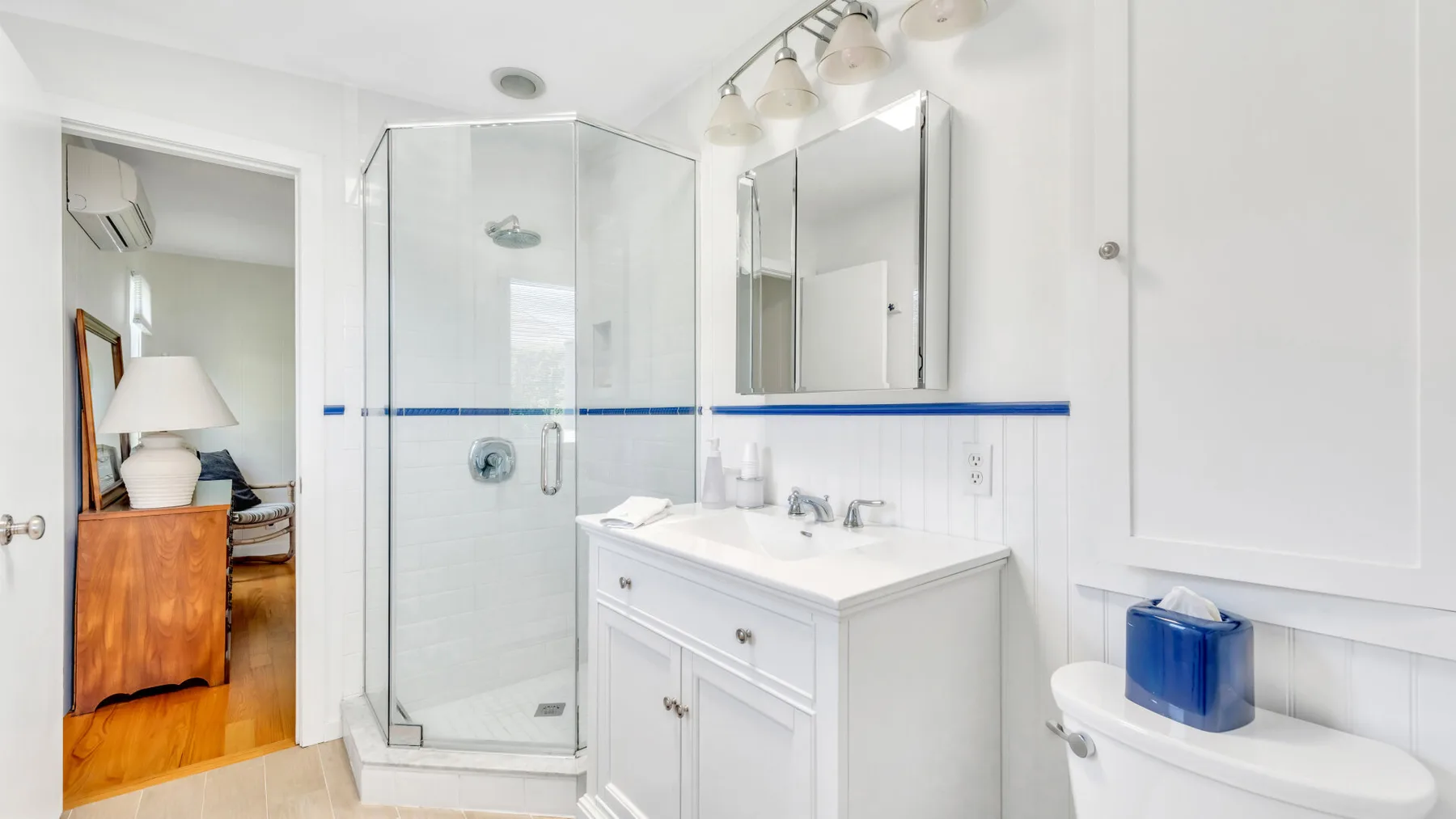 Un baño luminoso con una ducha de vidrio y un mueble de lavabo blanco.
