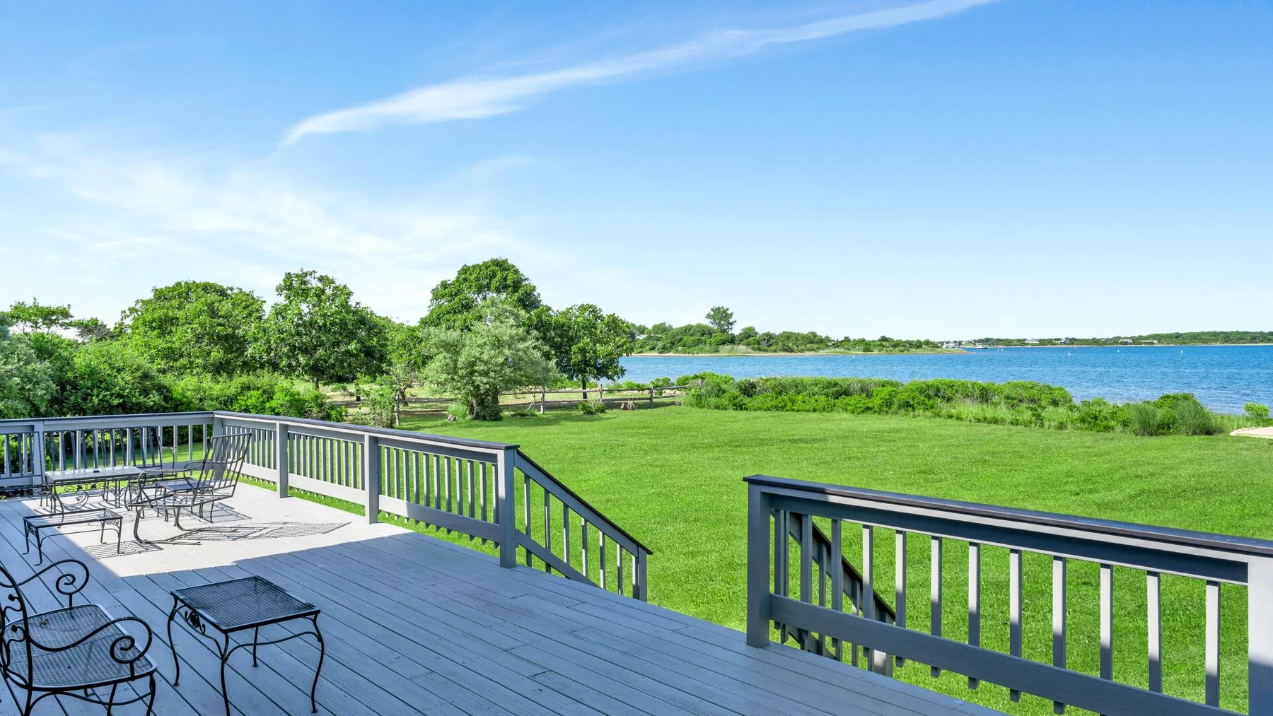 A deck overlooks a green lawn and a body of water.