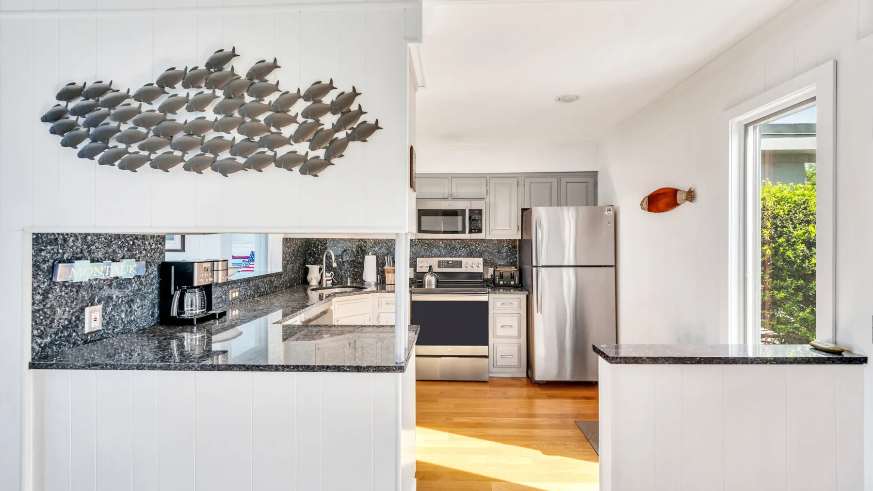 Una cocina luminosa con gabinetes blancos, electrodomésticos de acero inoxidable y una escultura de peces en la pared.