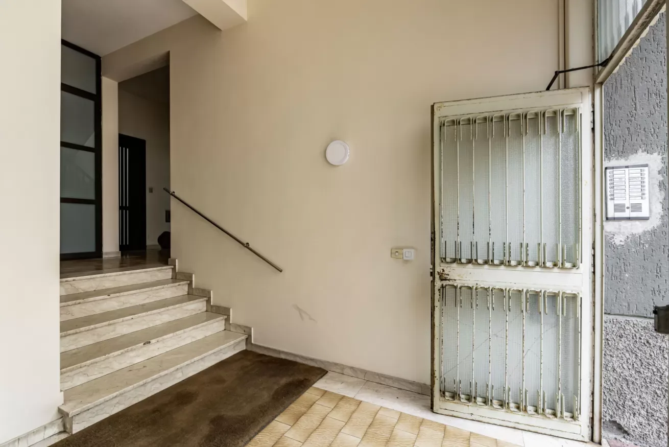 Una entrada de baldosas con una escalera corta y una puerta metálica abierta.