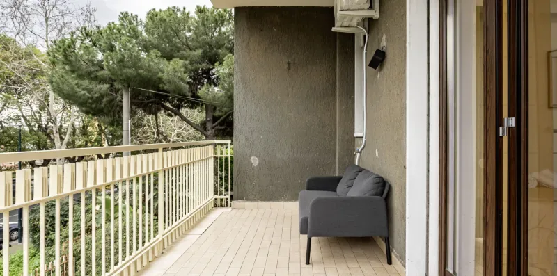 Un balcón con un sofá gris y una barandilla con vistas a los árboles.