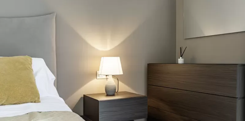 Un dormitorio con una cama, una lámpara de mesita y muebles oscuros.
