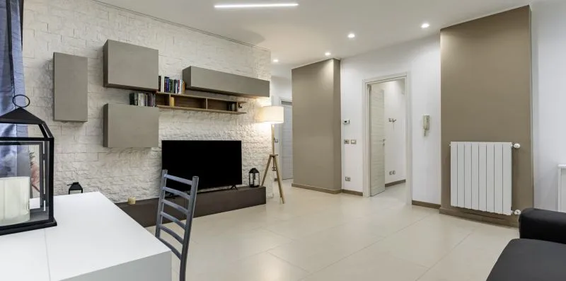 A modern living room with a television, wall shelving, and a dining table.