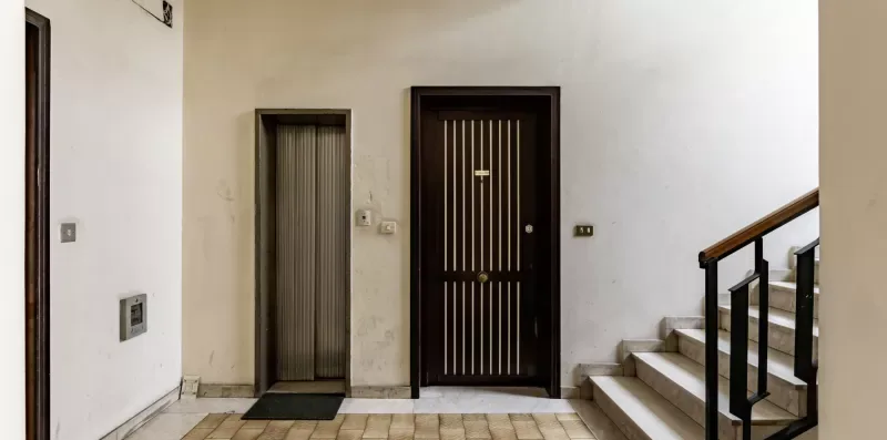 Una entrada interior con una puerta oscura y escaleras al lado.
