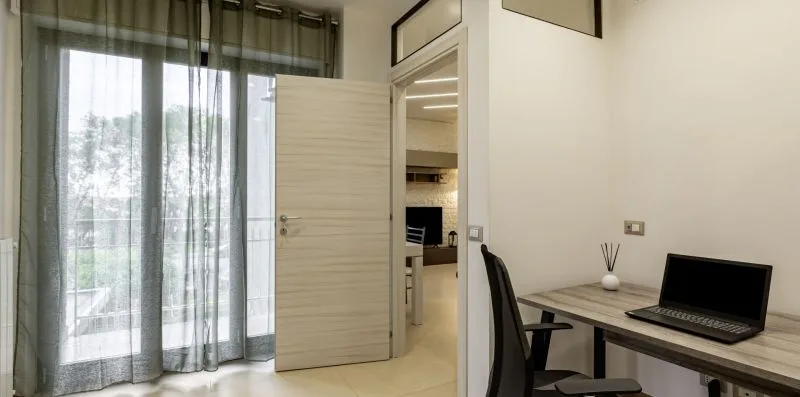 Una habitación luminosa con escritorio y portátil junto a una puerta abierta.