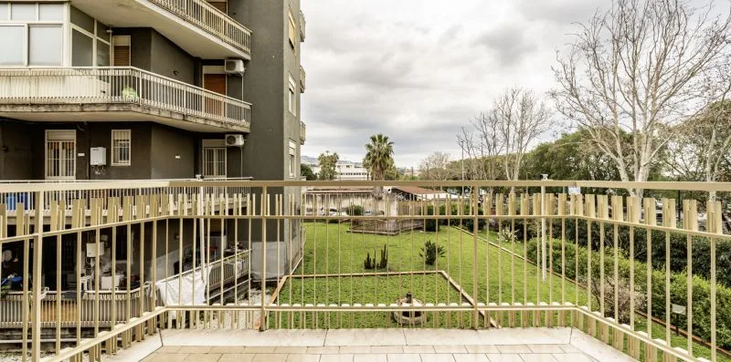 Un balcón da a un patio con césped y un edificio de apartamentos cercano.