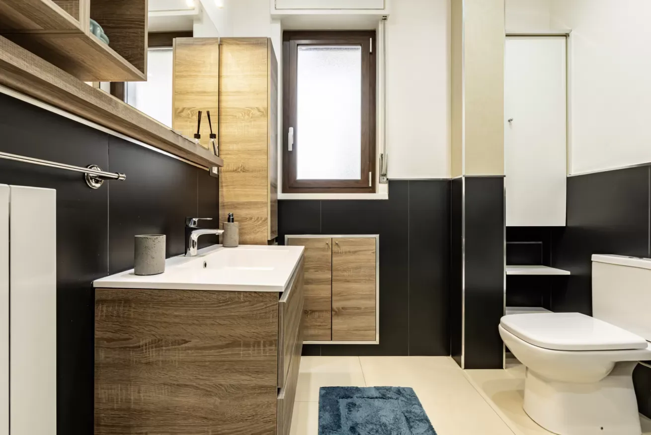 Un baño con lavabo de madera, lavamanos e inodoro.