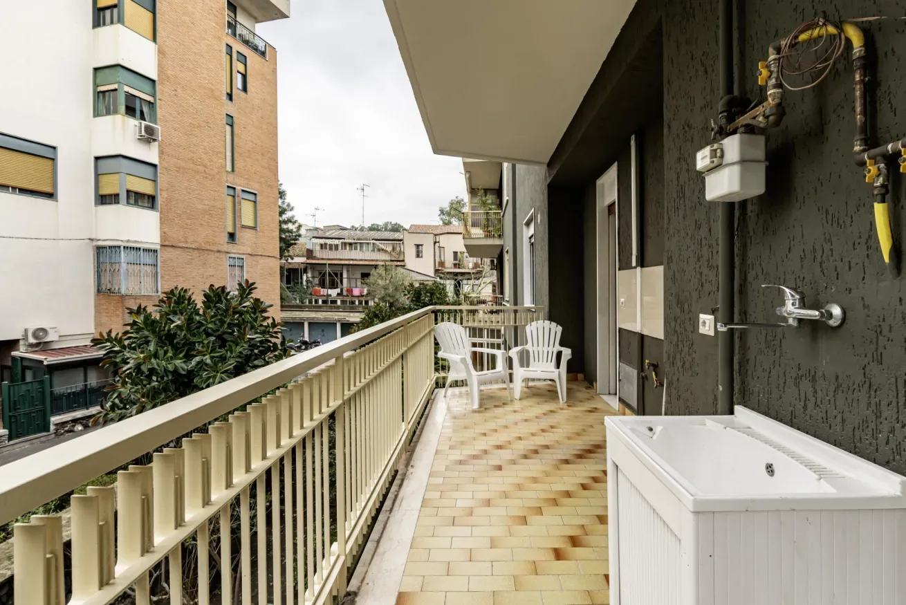 Un balcón largo con asientos al aire libre y una bañera blanca junto a la pared.
