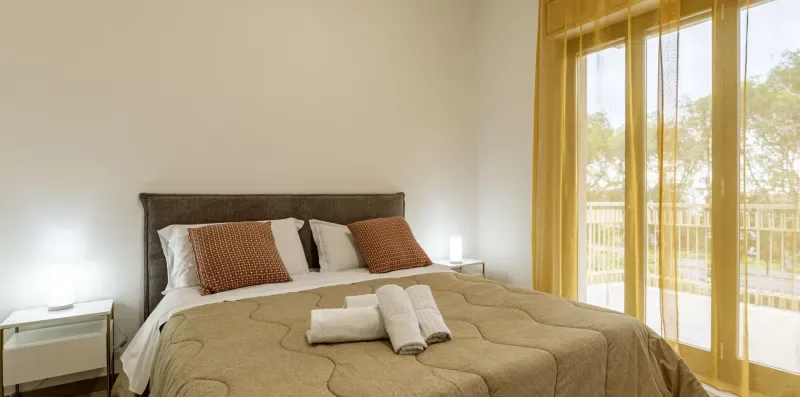 Un dormitorio con una cama bien tendida y ventanas grandes.