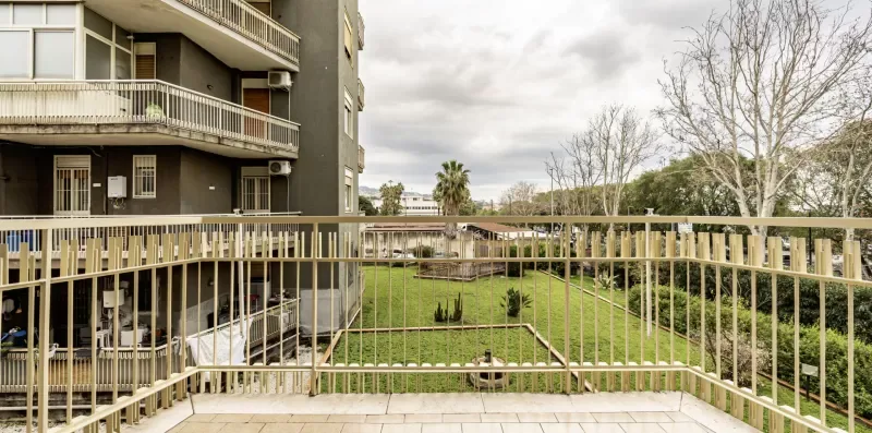 Un balcón da a un patio con césped junto a un edificio de varios pisos.