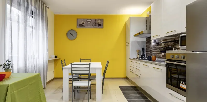 Cocina y comedor con armarios blancos, una mesa y una pared amarilla.