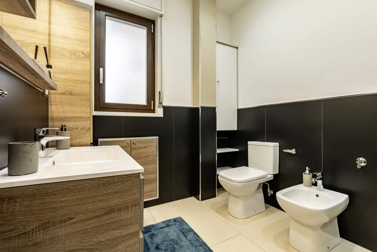 Un baño moderno con lavabo, inodoro, bidé y azulejos oscuros.