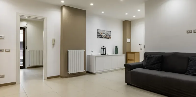 Una sala de estar con un sofá oscuro, un radiador blanco y un mueble bajo.