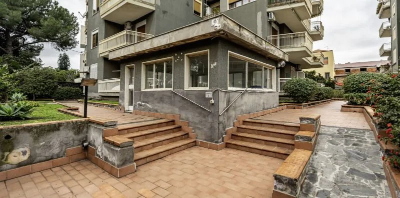 Sendero exterior y escalones junto a un edificio de varios pisos, con zonas ajardinadas.