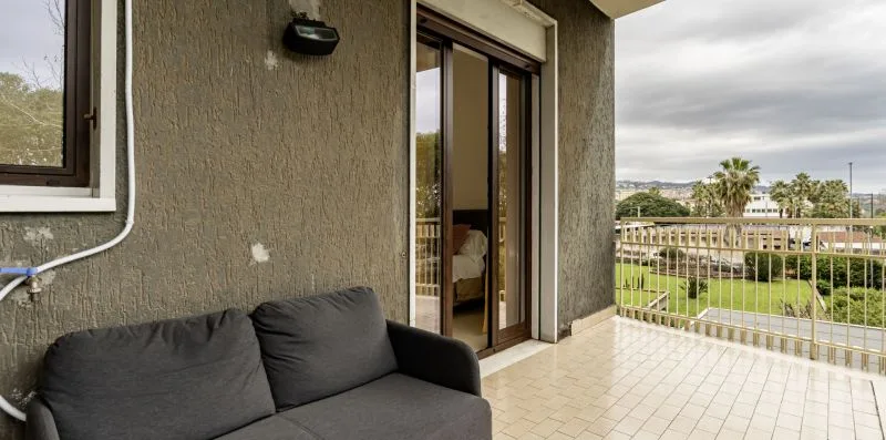 Un patio cubierto con asientos acolchados y vistas a los jardines.