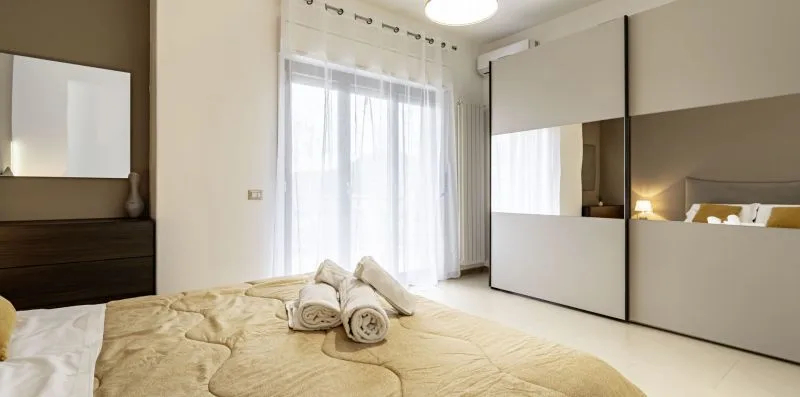 A bedroom with a bed dressed in light bedding and mirrored wardrobe doors.