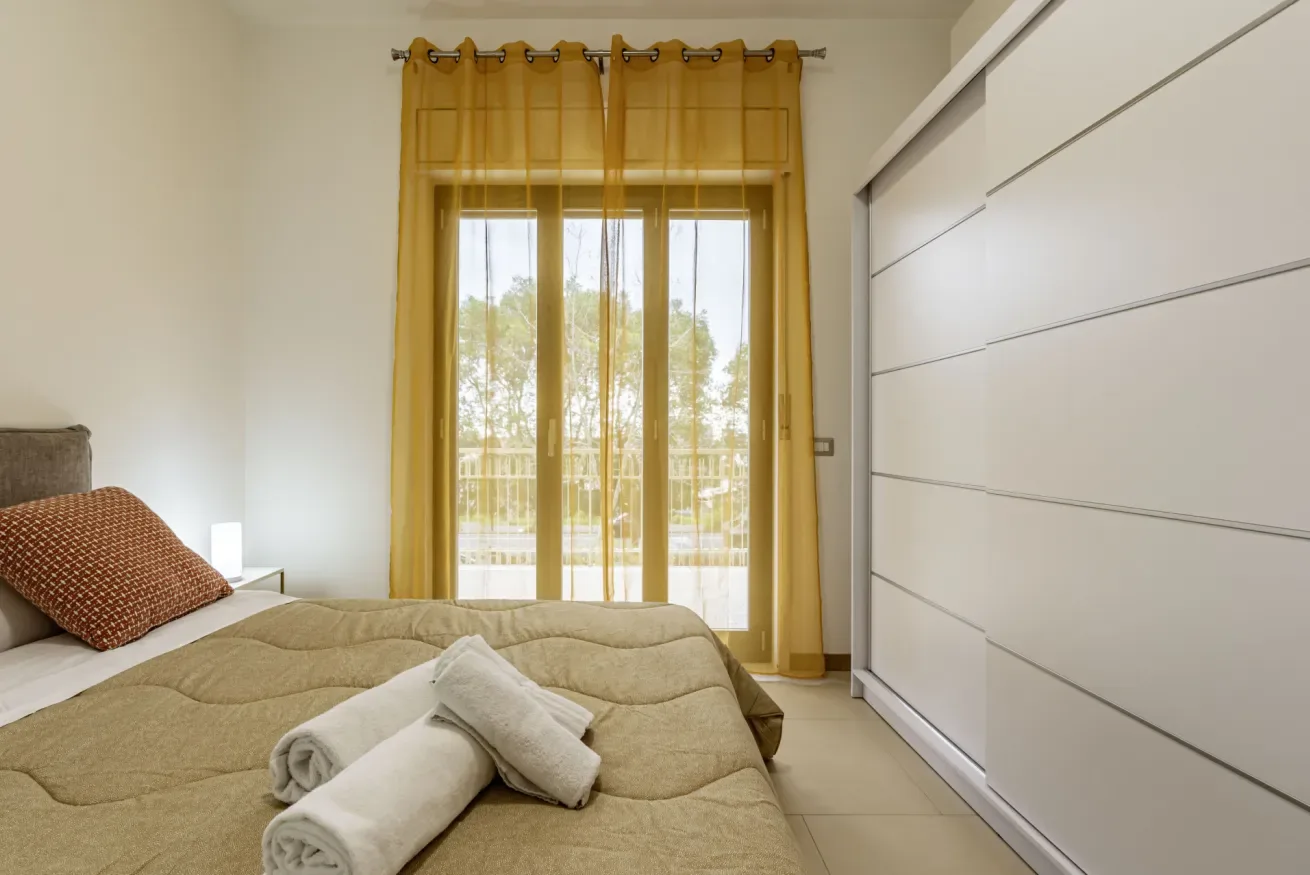 Dormitorio con una cama, toallas dobladas y una gran ventana con cortinas amarillas.