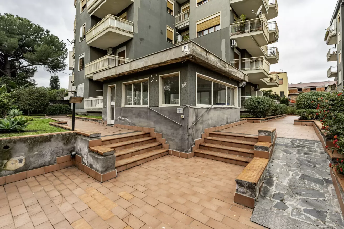 Un patio pavimentado junto a un edificio gris, con escaleras que conducen a la entrada.