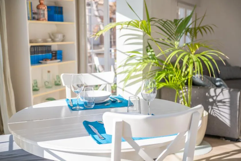 A bright dining area with a white table set beside a large potted palm.
