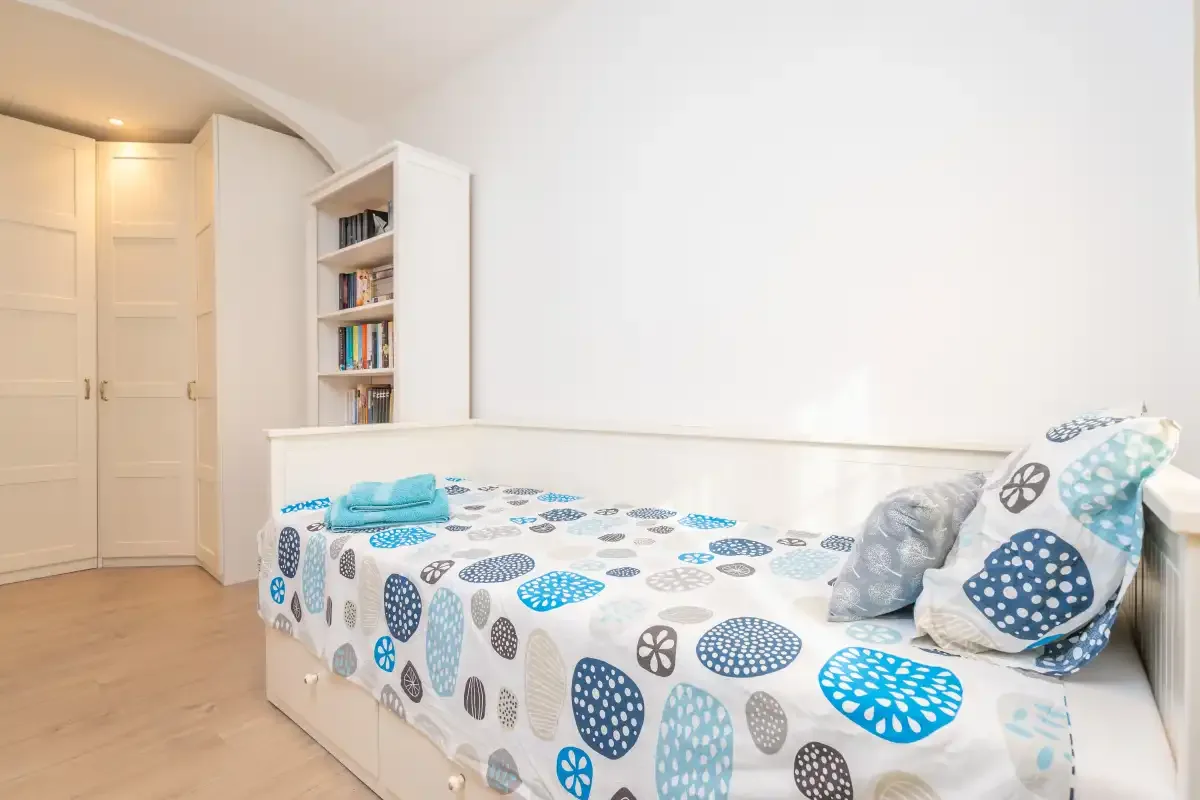 A bedroom with a bed covered in blue and gray patterned bedding beside a bookcase.