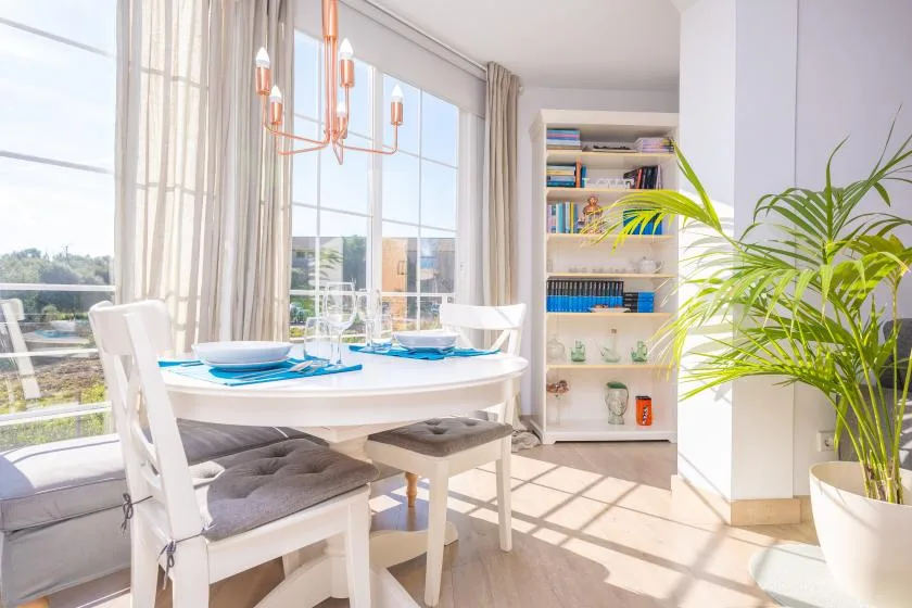 A bright dining area with a set table beside large windows and a bookcase.