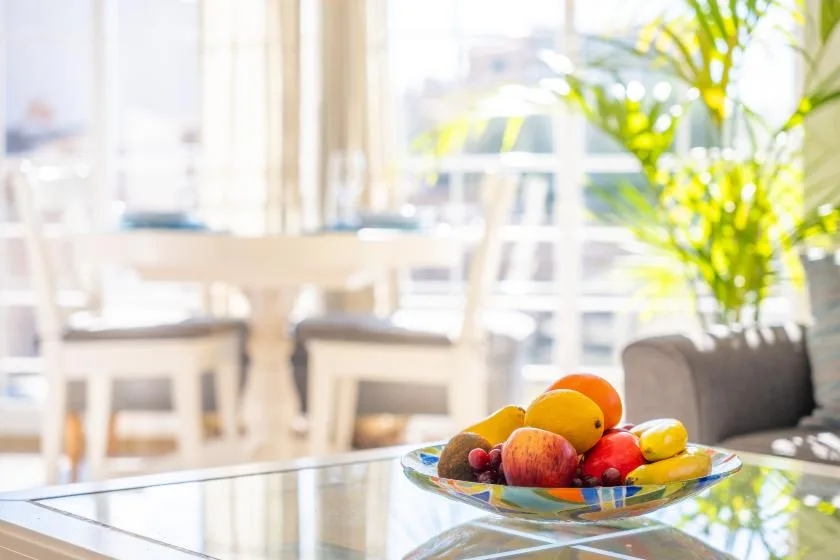 A bright dining area with a bowl of fruit on a glass table.