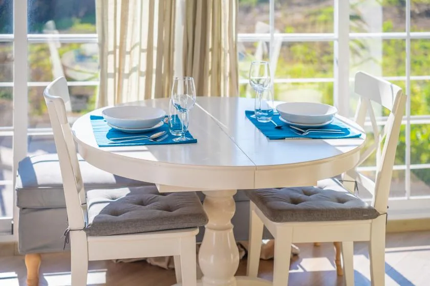 A dining table is set with blue placemats beside large windows.