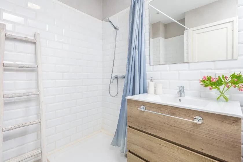 A bright bathroom with a wood vanity, mirror, and shower curtain.