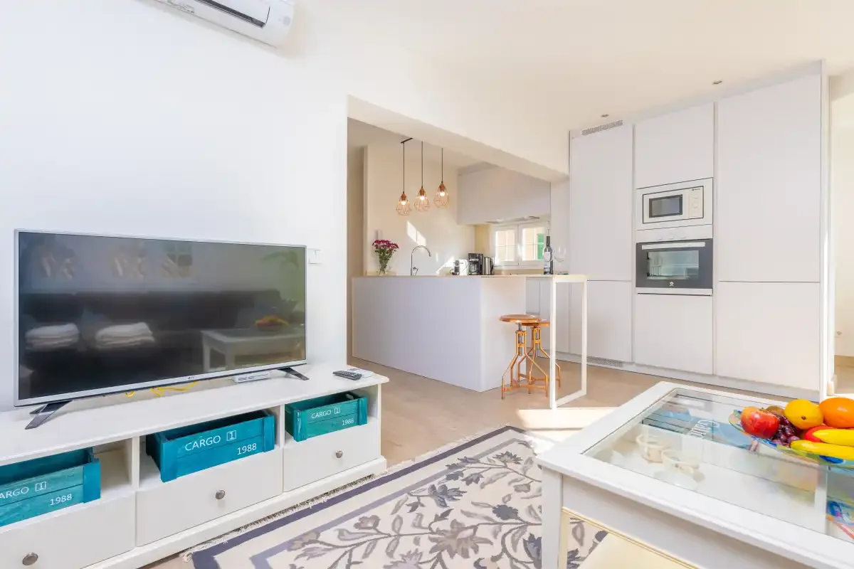 A bright living area opens onto a compact kitchen, with a television and glass coffee table.
