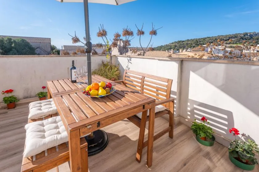 A sunny terrace has a wooden dining table with fruit and cushioned seating.