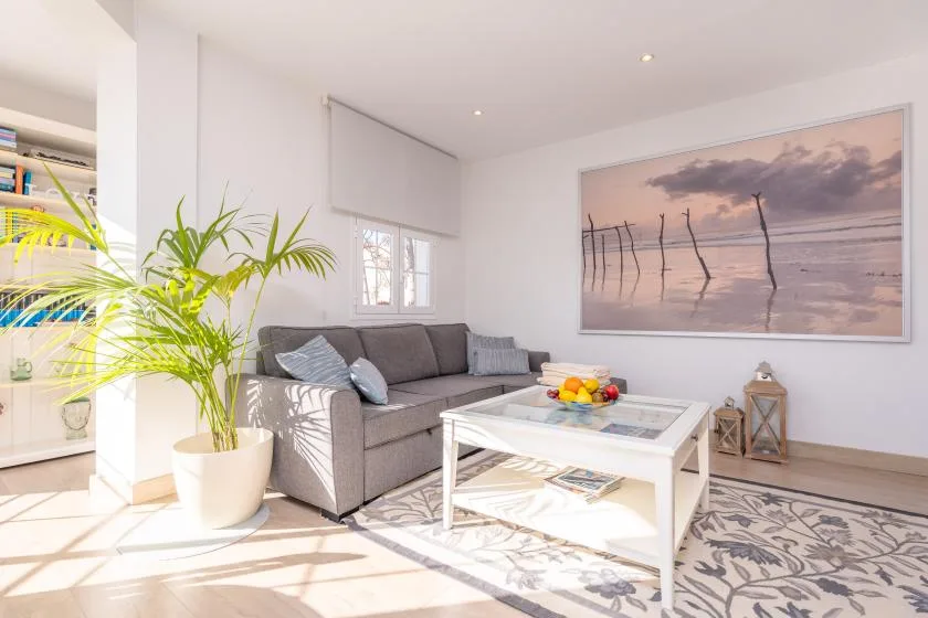 A bright living room with gray seating, a white coffee table, and a large beach photograph.