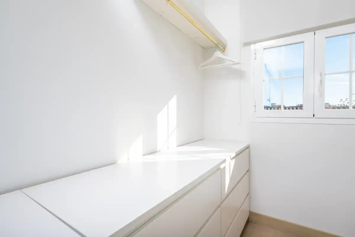 A bright white room with a long built-in counter beneath a window.