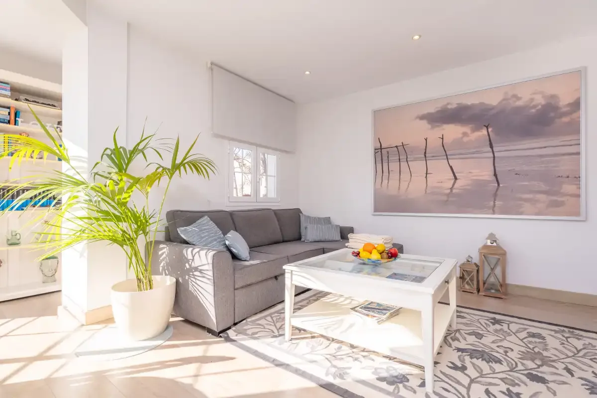 A bright living room with gray seating, a white coffee table, and a large beach photograph.
