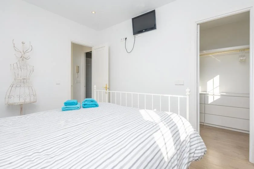 A bright bedroom with a striped bedspread and a wall-mounted television.