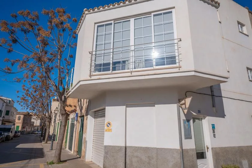 A white two-story building stands on a sunny street beneath a clear blue sky.