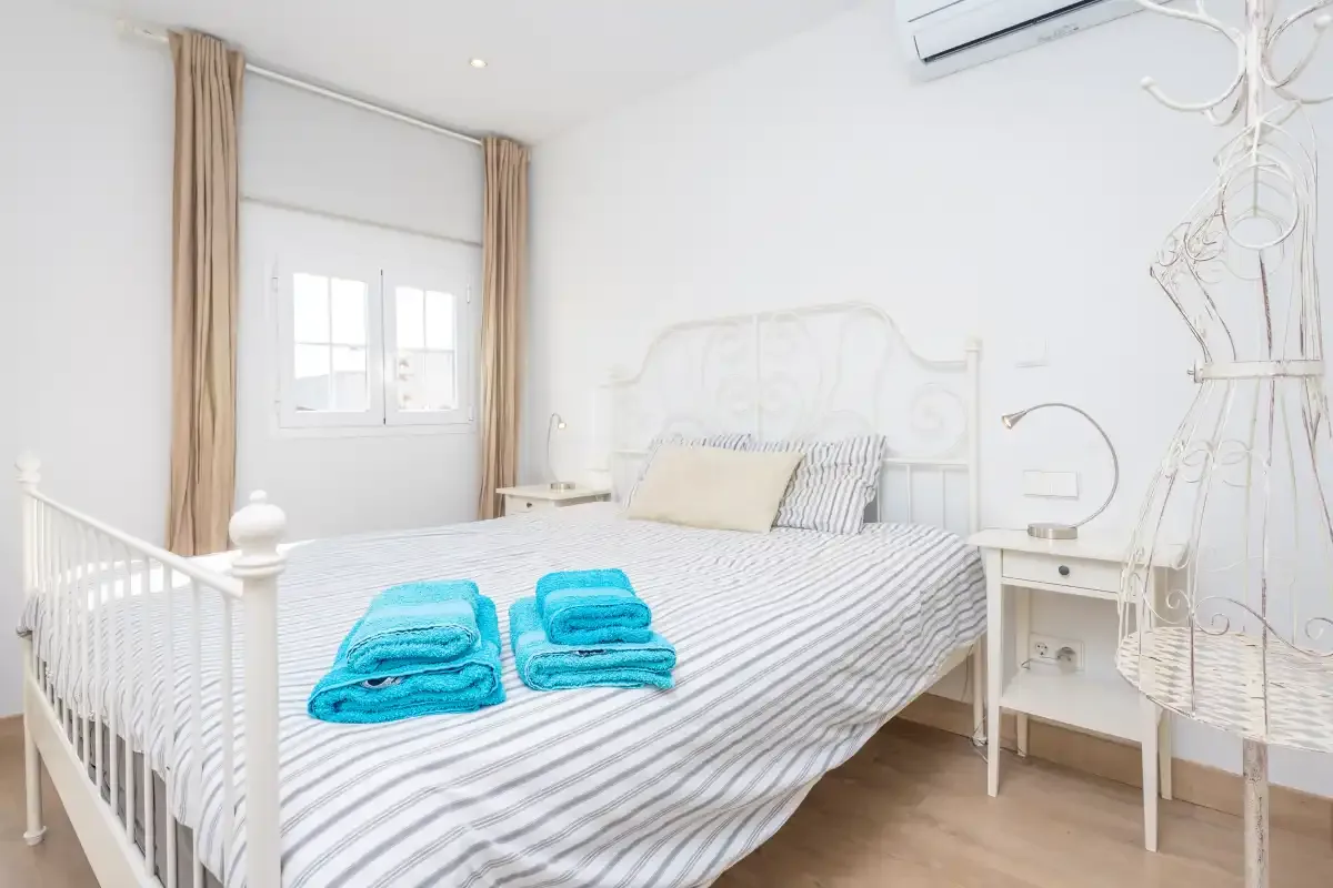A bright bedroom with a striped bed and folded turquoise towels.