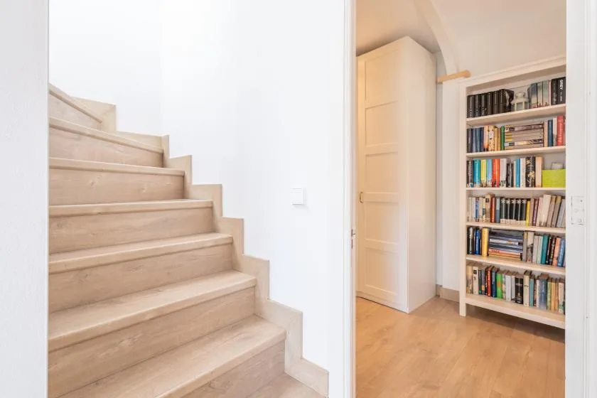 A bright interior hallway with a staircase and a bookcase.