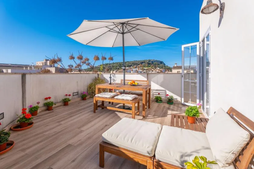 A rooftop terrace with outdoor seating, a large umbrella, and potted plants.