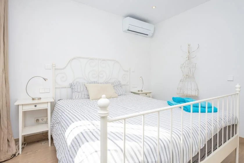 A bright bedroom with a white bed, striped bedding, and an air conditioner.