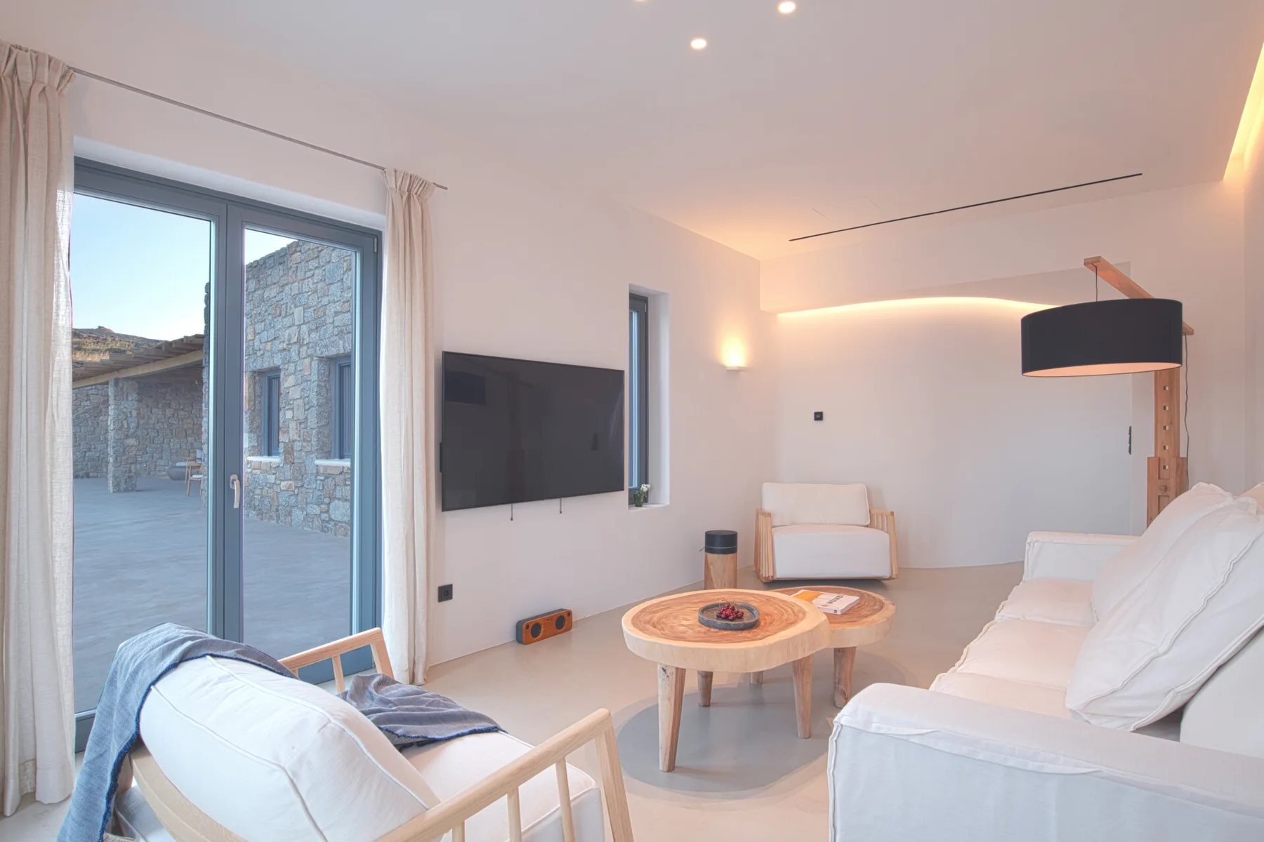 Una sala de estar luminosa con asientos, una mesa de centro y un televisor en la pared.