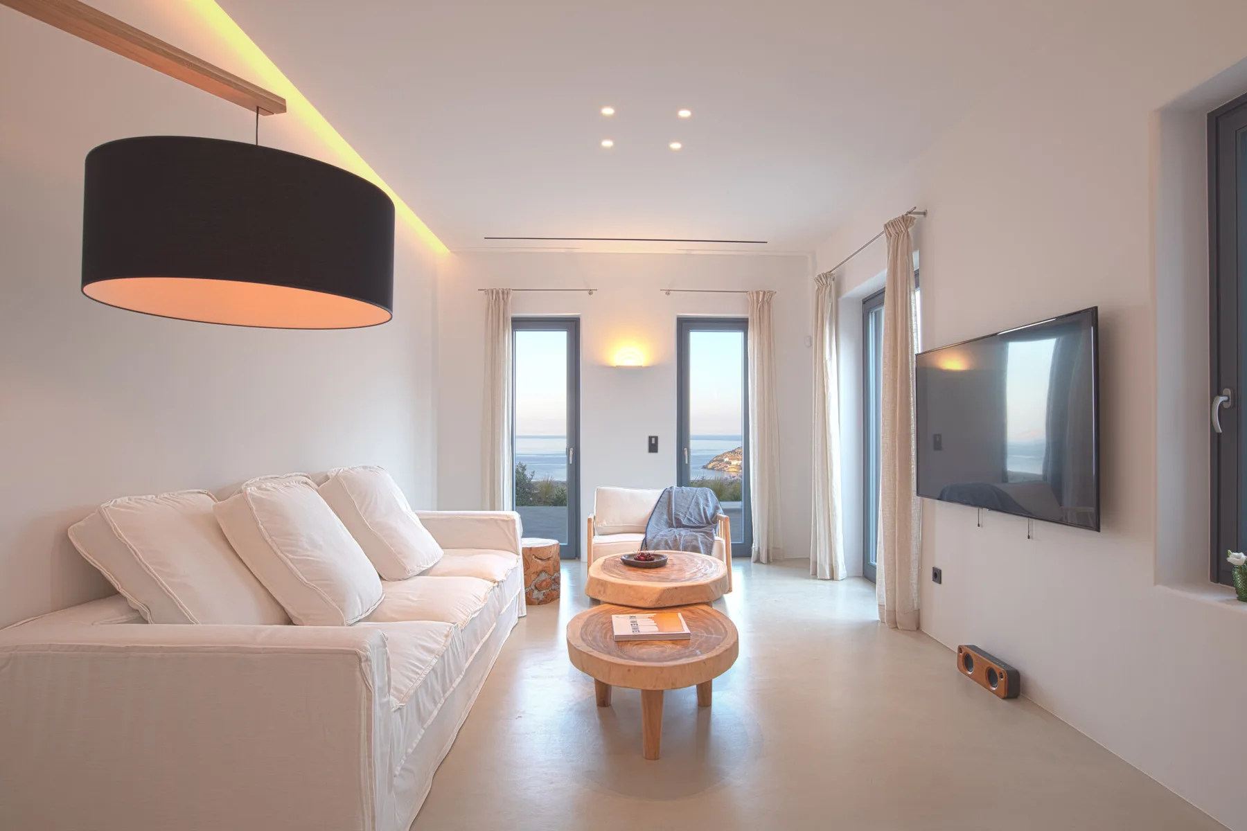 A bright living room with light seating, coffee tables, and a wall-mounted television.