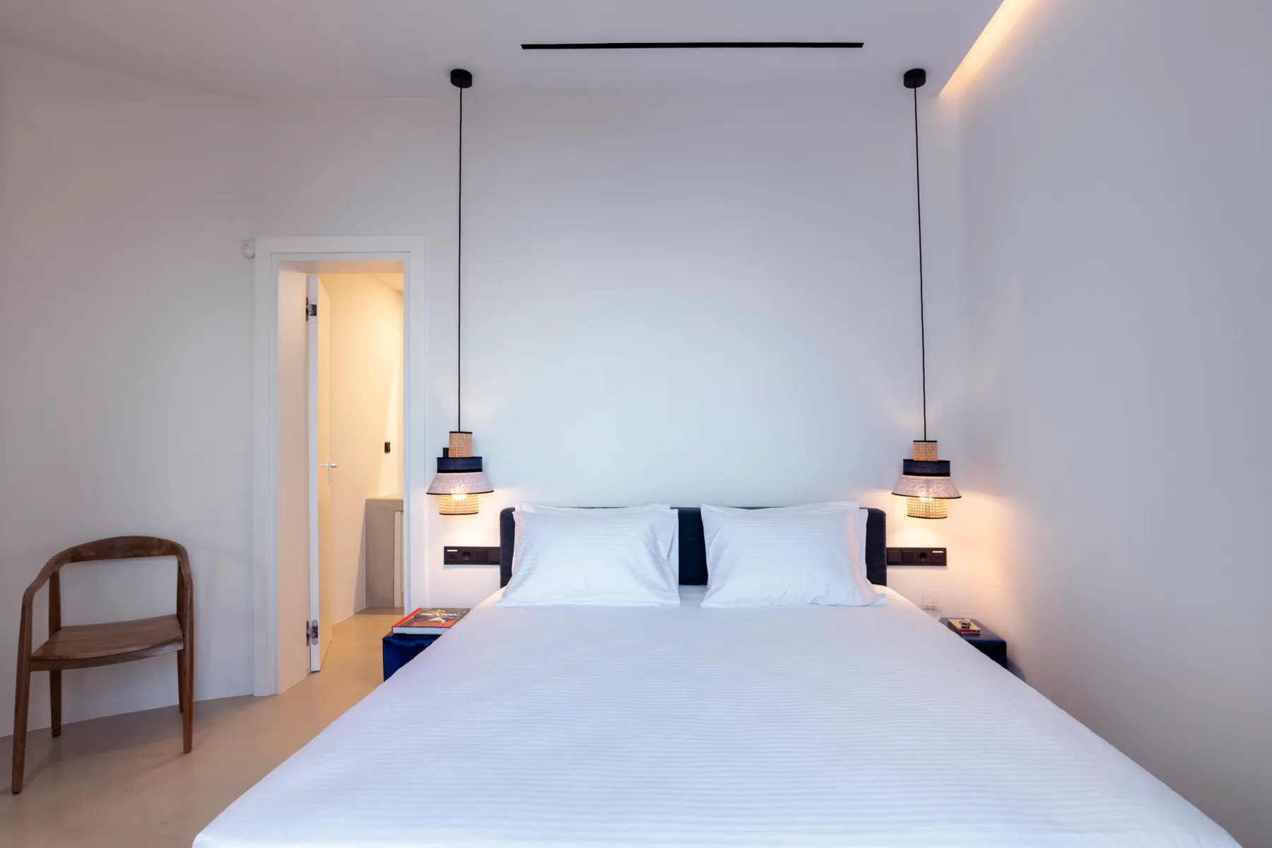 A bright bedroom with a neatly made bed and pendant lights.