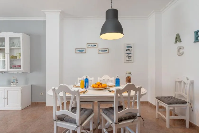 A bright dining room with a white table and chairs beneath a pendant light.