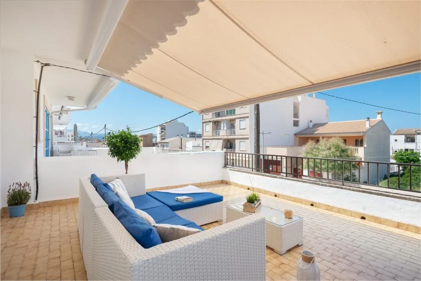 A sunny rooftop terrace has blue-cushioned seating beneath a retractable awning.