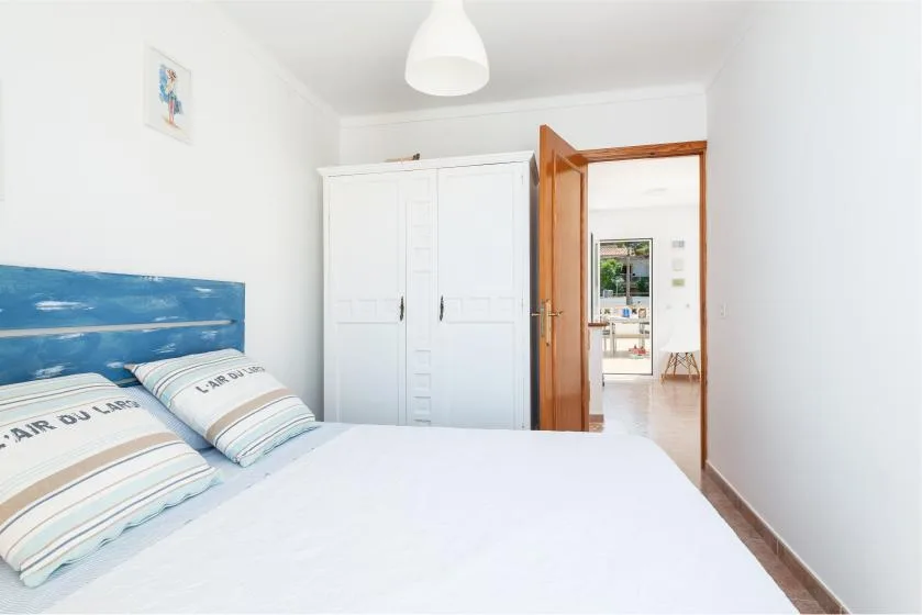 A bedroom with a bed, blue headboard, and white wardrobe beside an open doorway.