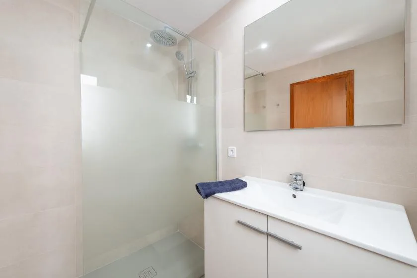 A bright bathroom with a glass shower and a long white vanity.