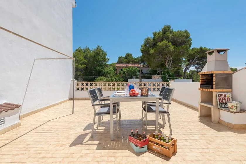 A sunny rooftop terrace has a dining table and chairs beside an outdoor grill.