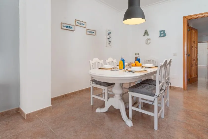 A dining area with a white table, chairs, and a pendant light.